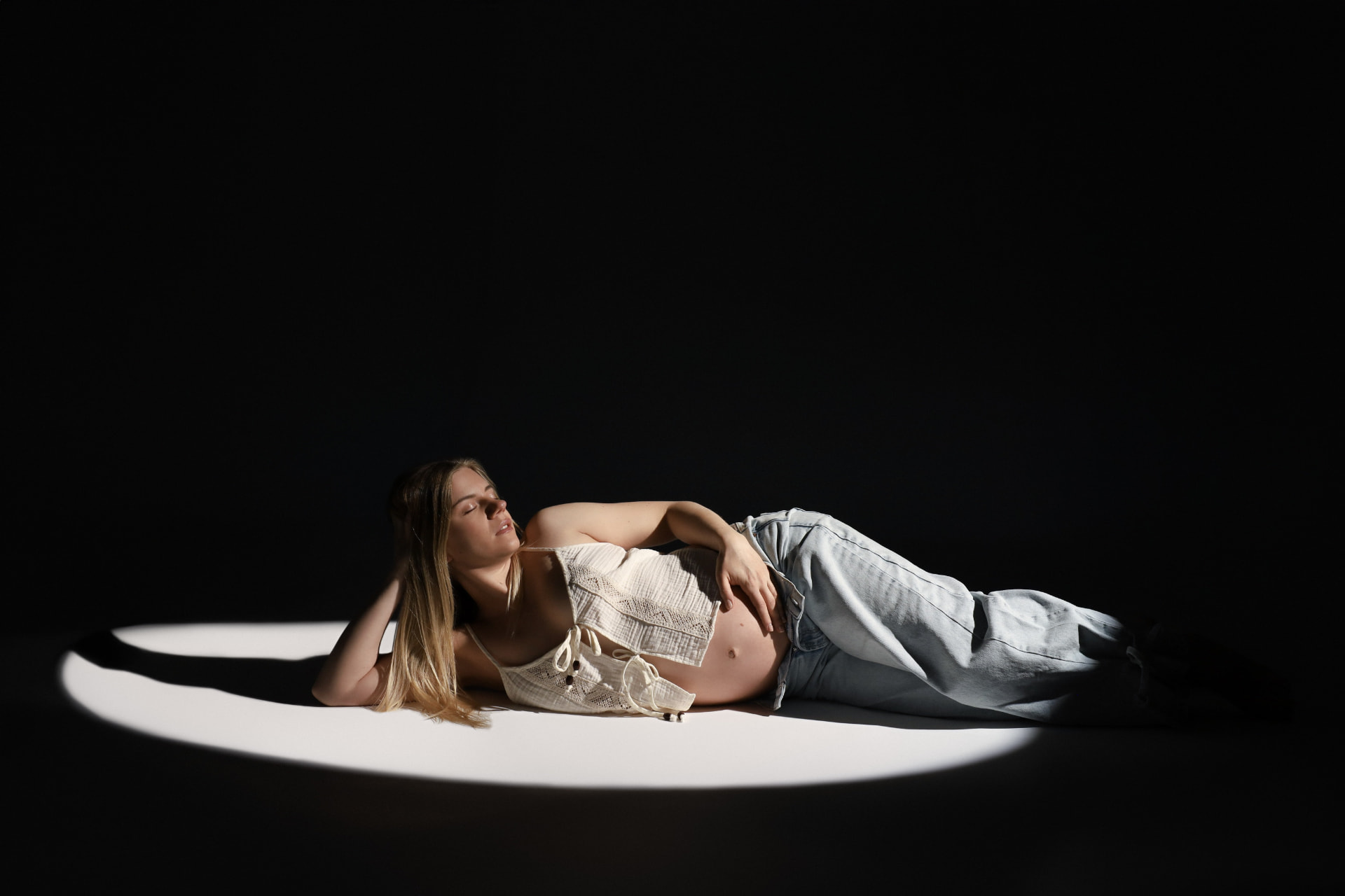 Zwangere vrouw liggend in een lichtcirkel op een donkere studioachtergrond