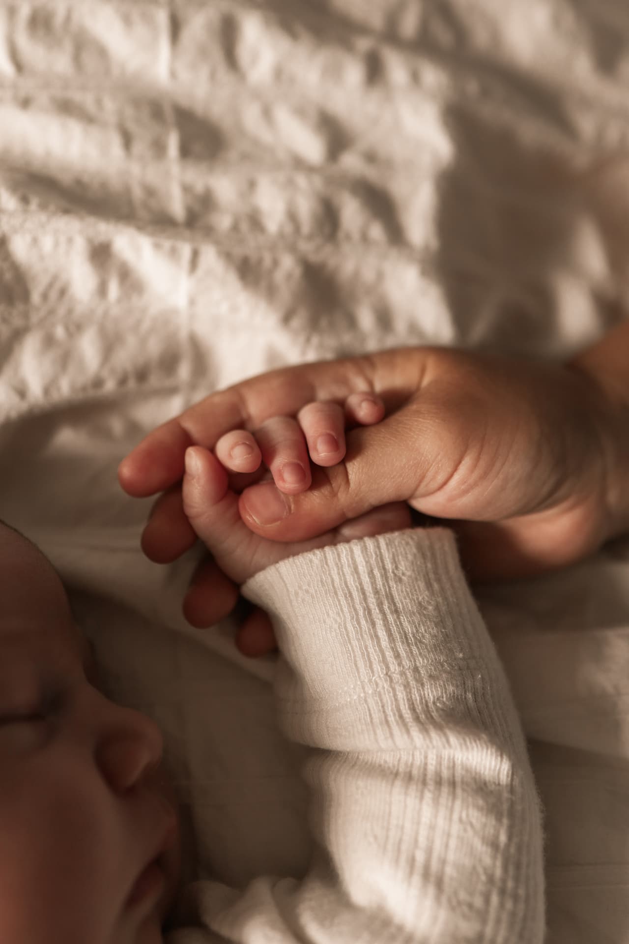 Slapende pasgeboren baby op een crèmekleurige deken, terwijl een volwassen hand het handje vasthoudt