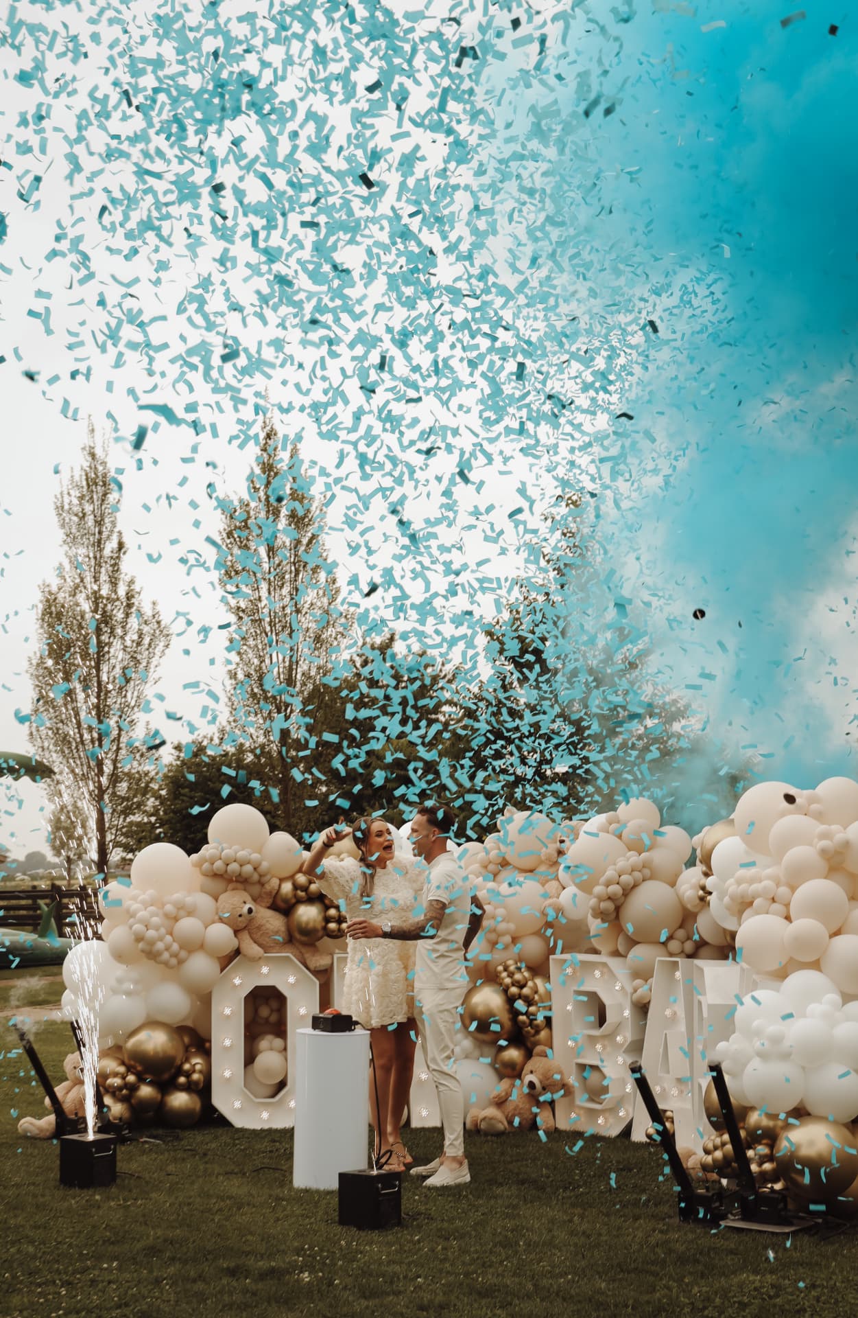 Stel viert een gender-reveal met blauwe confetti voor een ballonnenwand