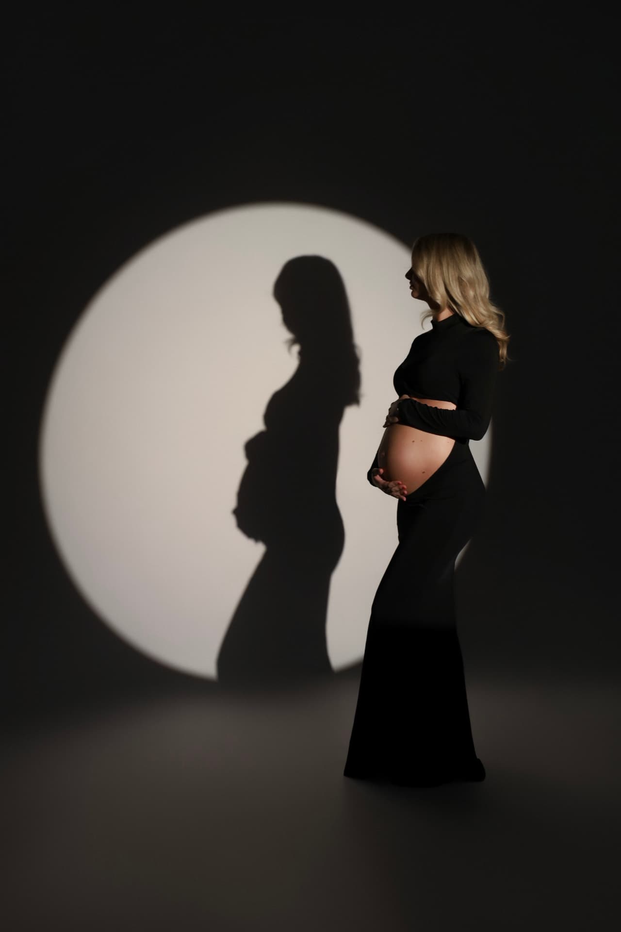 Zwangere vrouw in het zwart met haar schaduw in een lichtcirkel